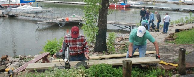 work party, wood working with a chopsaw, 2 men plaid shirts, nice day
